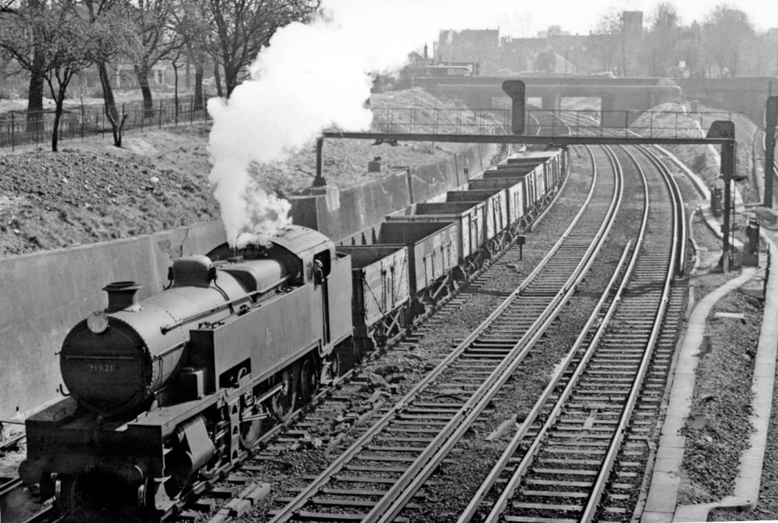 Up mineral empties on Brighton line approaching Clapham Junction
22nd March 1957
The train has come from Norwood Yard (via either Crystal Palace or Selhurst) and is probably bound for Willesden LMR by the West London Line. With its rear still passing under Battersea Rise overbridge, it is hauled by one of the Maunsell W class 2-6-4Ts which were entirely devoted to cross-London freight exchange work, no.31921 (built October 1935, withdrawn June 1963).
© Ben Brooksbank (CC-by-SA/2.0)
