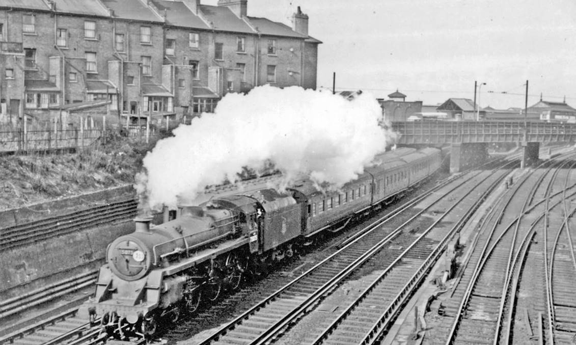 Waterloo - Basingstoke train pulling away from Clapham Junction
2nd April 1958
Not many years before the Bournemouth line electrification, in the final steam-hauled years the important 'commuter' services from Basingstoke were handed over from the traditional old LSWR engines to new BR Standard 4-6-0 types. 
Class 4MT no.75075 (built November 1955, withdrawn July 1967) is about to pass south under Battersea Rise bridge
© Ben Brooksbank (CC-by-SA/2.0)
