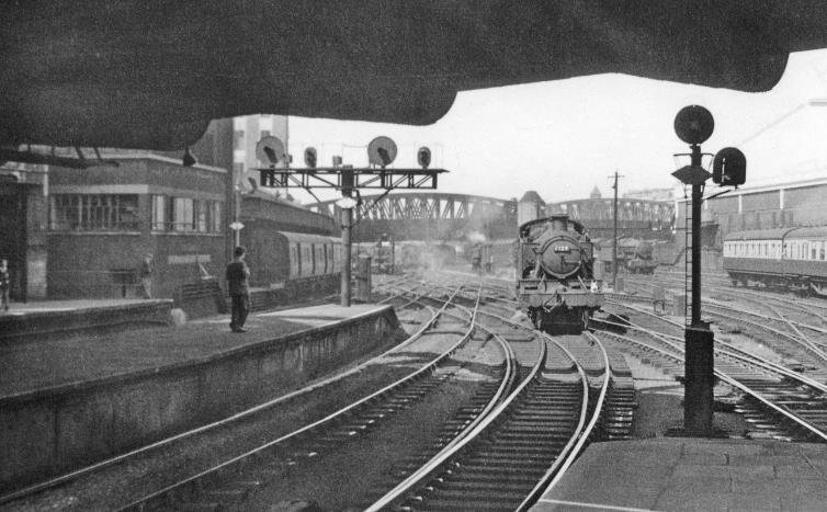 BloodandCustard
Paddington Station
Paddington Station, exit on Departure side
25th July 1953
From the end of Platforms 4/5 underneath Bishops Road Bridge to Westbourne Bridge. On the left is the Departure Box and beyond it the Parcels station. Several locomotives are coming and going, the nearest being Prairie tank no. 6119.
© Ben Brooksbank (CC-by-SA/2.0)
