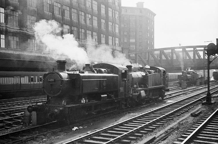 BloodandCustard
Paddington Station
Outside Paddington Station 
April 1960
A variety of locomotives waiting to take up duty, mainly for empty stock working out to Old Oak Common depot. The nearer locomotive is one of the 9400 class and represents the final development of the pannier style tank locomotive for shunting duties, developed as late as 1948, and mainly built under the British Railways regime.
Next to the  9400  is one of the 5100 class large Prairie tank locomotives which may well be waiting to take a commuter service out of Paddington rather than empty stock.
 Of interest is the passenger vehicle visible to the left. This is distinctively of LNER origin and some way from its normal territory. It is standing in the long parcels bay which extended out beyond platform 1 of Paddington Station. 
  Alan Murray-Rust (CC-by-SA/2.0)