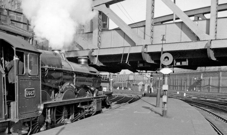 BloodandCustard
Paddington Station
'Capitals United Express' ready to leave Paddington
13th April 1962
The Down 'Capitals United Express' will leave at 8.55am, with 'Castle' no.5087 'Tintern Abbey' (rebuilt November 1940 from 'Star' no.4067 of January 1923, withdrawn August 1963). The train will arrive at Swansea at 1.25pm, reverse and continue to Neyland (arr. 4pm) and Milford Haven (arr. 4.15pm), the portions dividing at Johnston. 
Just above is Bishop's Bridge; beyond and over the Up main and local lines and the Underground (Hammersmith & City) lines is the great Paddington Goods Station. Note the adjacent  searchlight  signal with Rule 55 exemption plate.
  Ben Brooksbank (CC-by-SA/2.0)
