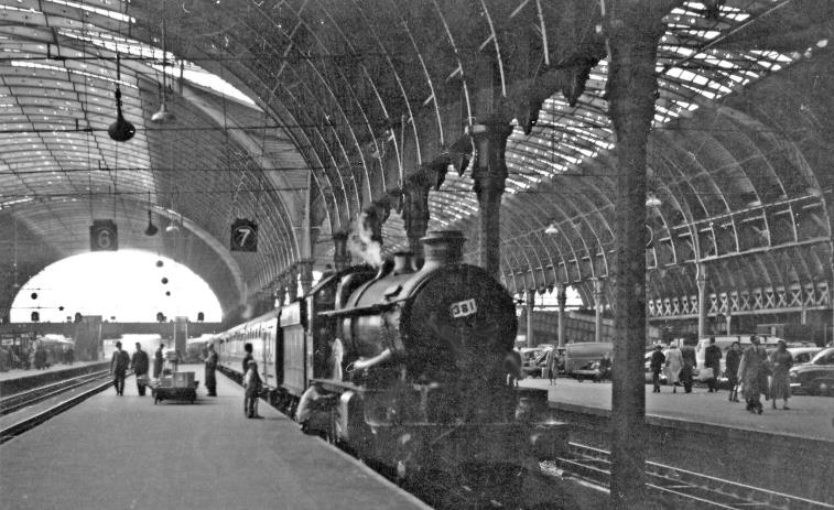 BloodandCustard
Paddington Station
Platform 6/7 at Paddington
27th April 1963
From near the barriers at Platform 6/7 'Castle' no.7000 'Viscount Portal' (built May 1946 with modifications - named after the wartime Chief of the Air Staff, never after a Castle, withdrawn December 1963) has arrived with the 10.5am express from Hereford. 
 A father and son examine 7000's footplate admiringly, while the Driver stoops down to (probably) look for the cause of that knocking noise he had heard. Beyond Platform 9 on the right is the cab-road: the cars seem old - but the people are well-dressed. Not much sun is coming through Brunel's great roof. 
  Ben Brooksbank (CC-by-SA/2.0)