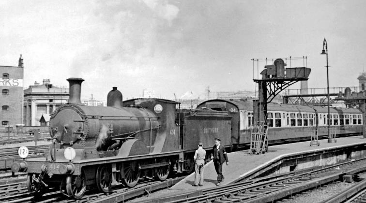 Ex-LSWR L11 working empty stock at Waterloo
24th June 1950
From the end of the main-line platforms at Waterloo on a Summer Saturday, when all sorts were put to work on steam expresses and their stock. This is Drummond L11 class no.414 (built July 1906, withdrawn April 1951) and still in Southern livery. 
Bulleid 5-set no.848 was outshopped new in CLC livery 17th April 1950, received BR(S) green 12th September 1958 and was disbanded in 1966.
“To the right behind the signal gantry can be seen the Shot Tower, prominent until demolished when the South Bank was redeveloped for the Festival of Britain a year later”.
© Ben Brooksbank (CC-by-SA/2.0)
