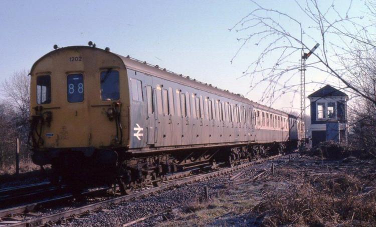 Illuminated by some bright morning sunshine, 3R unit no.1202 starts away from Edenbridge on Saturday 3rd February 1979 working a Tonbridge to Reading train with the 'eight wheel driving cab' leading! At this date the unit was misformed, running for a while with 6L trailer 60551 (borrowed from unit no.1031) and it has two four-bay passenger saloons whereas a genuine 6S car had a three-bay saloon adjacent to the toilet end. The signalman is visible inside the neat little SER style box, about to drop the starter back to danger behind the train, a nice short pull there! Unit nos.1202 own TSO 60504 was at Selhurst being repainted into blue /grey at this time.
© John Atkinson

