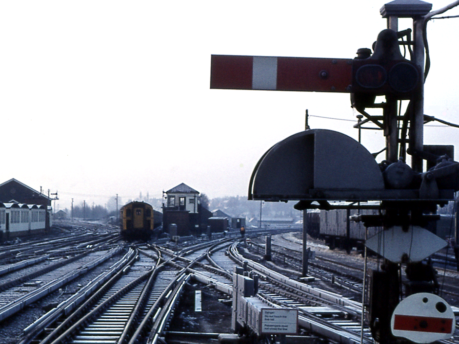 https://www.bloodandcustard.com/BR-4VEP.html
A pair of 4 VEP units take the road into Redhill’s platform 2 on 28th January 1976.
The signal, its three-way mechanical route indicator and subsidiary aspect (also in the background Redhill ‘B’ signal box) all had less than a decade of service left. Note the conductor rail running through the boarded staff crossing from platform 3.
© Tony Watson