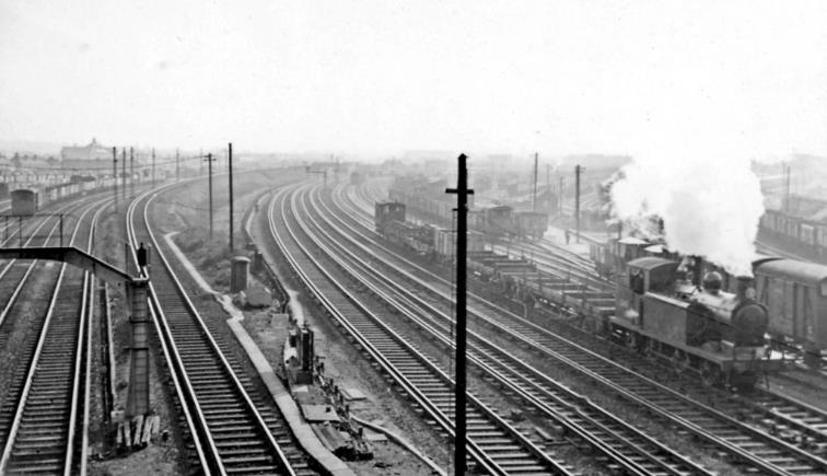 View South from Tennyson Road bridge on 2nd April 1958. The Down and Up Norwood marshalling yards are on each side and the Norwood Loop round to Selhurst is on the right behind the Up goods train, which is headed by E6 no. 32413.
 Ben Brooksbank (CC-by-SA/2.0)
