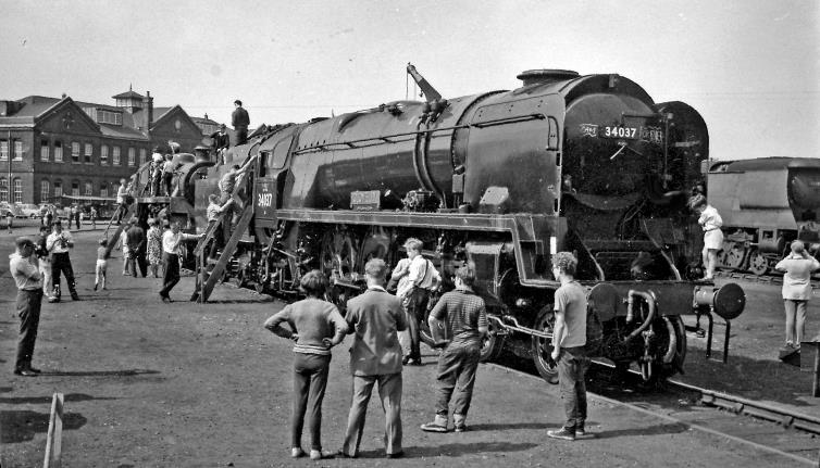 With its cab open to the public, sitting in Eastleigh Yard is freshly-repaired rebuilt Bulleid Light Pacific no.34037 'Clovelly' (built August 1946 as no.21C137, renumbered March 1949, rebuilt March 1958, withdrawn July 1967) is the subject of numerous young male admirers - who are also swarming round a BR Standard 4-6-0 beyond. In the background is the main office building of the Works.
 Ben Brooksbank (CC-by-SA/2.0)
